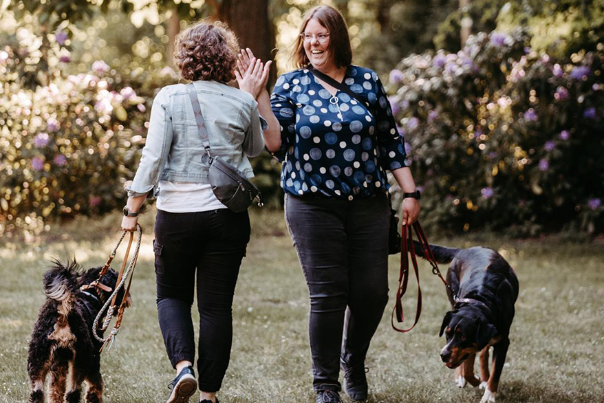 Zwei Freundinnen mit zwei Hunden klatschen ab